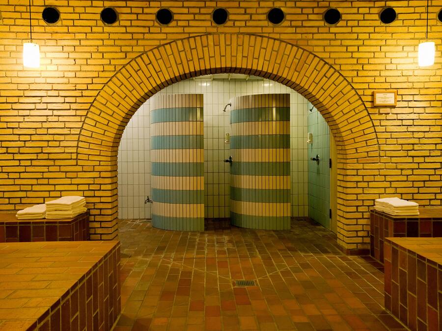 A public restroom with a brick archway, tiled walls, and benches with towels.