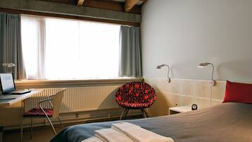A hotel room with a bed, a desk with a laptop, a chair, and a window with curtains.