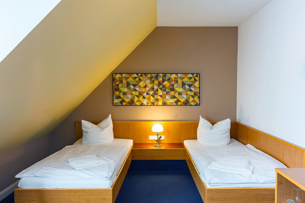 A hotel room with two beds, a wooden headboard, a blue carpet, and a geometric wall art piece.