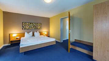 Une chambre d’hôtel avec un grand lit, deux tables de chevet avec des lampes, une armoire en bois et un tableau abstrait aux couleurs vives accroché au mur.