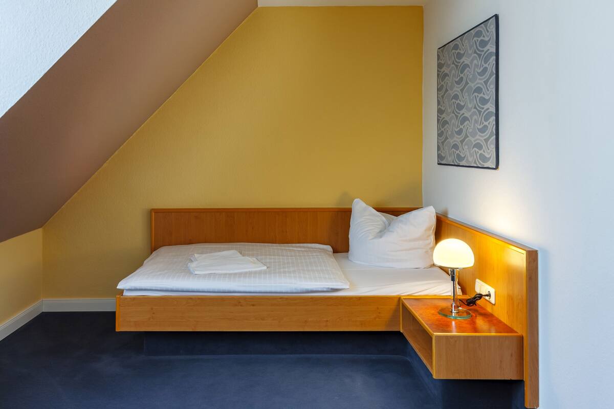 A neatly made bed with a wooden headboard, a bedside lamp, and a framed artwork on the wall.