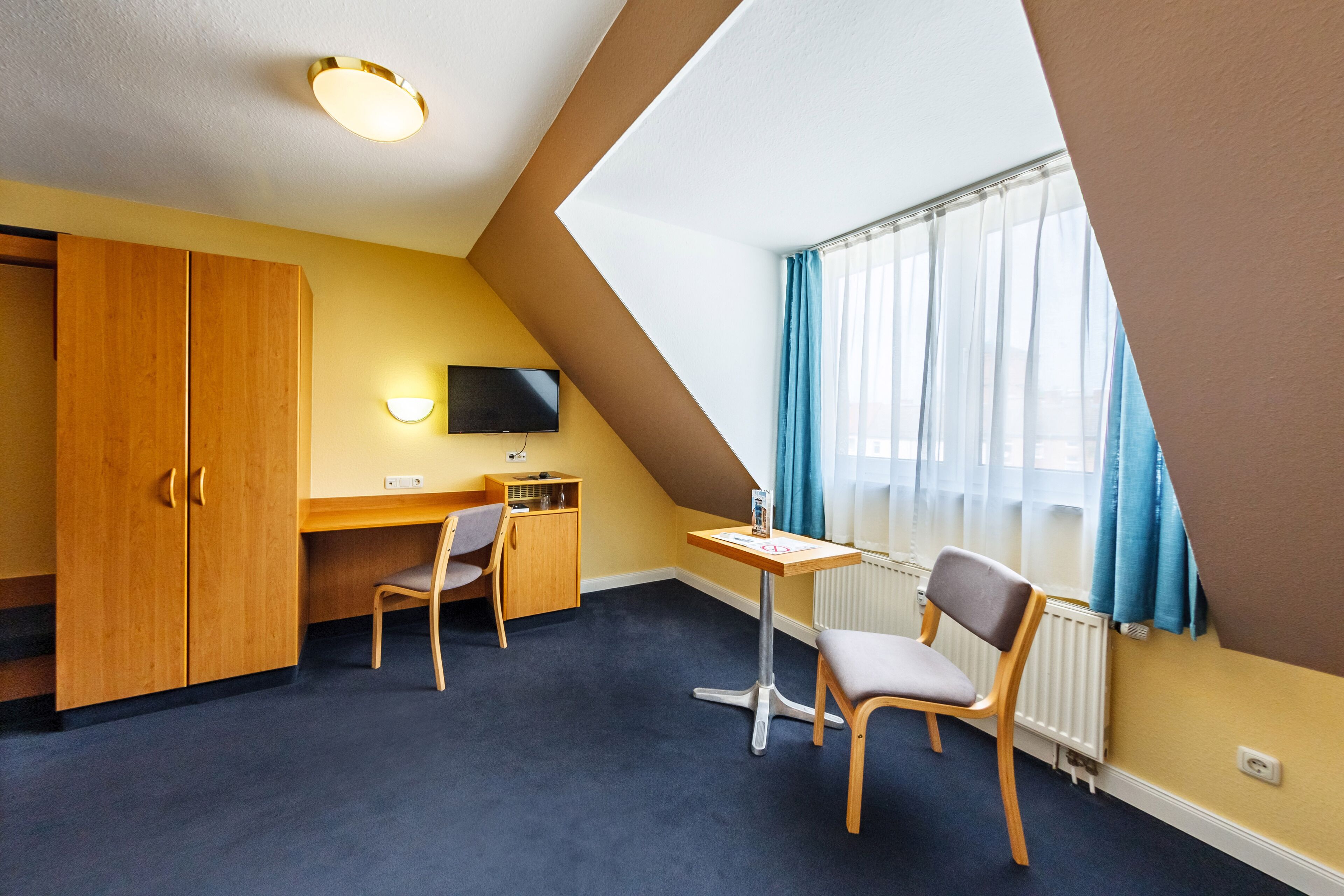 A room with a desk, two chairs, a television, and a window with curtains.