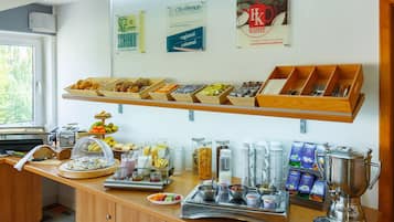 A breakfast buffet with various food items and beverages, a coffee machine, and a sign indicating a seasonal menu.