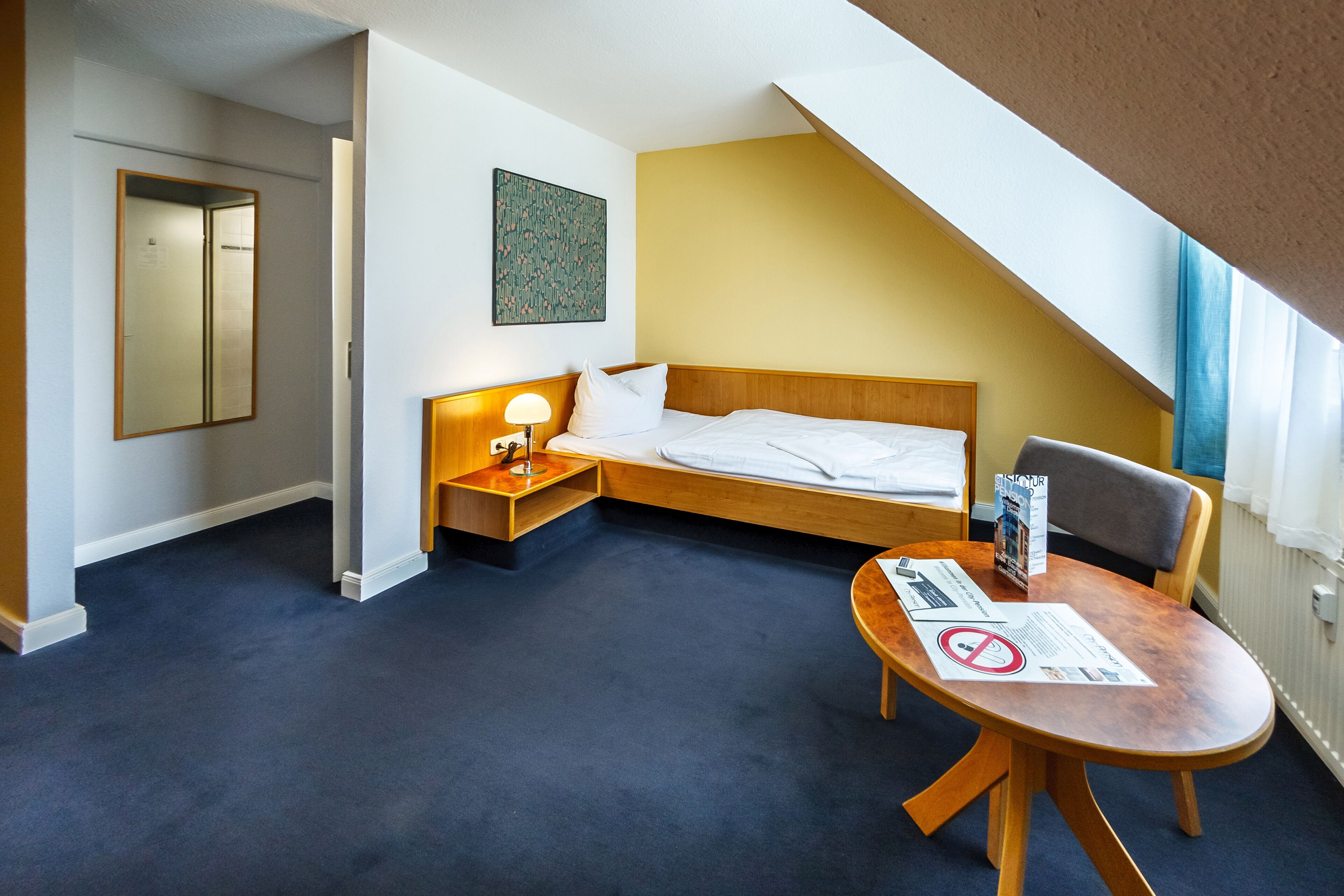 Una habitación de hotel con cama, mesita de noche, lámpara y una pequeña mesa con un menú.