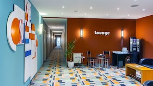 Un hall d’hôtel avec un sol aux motifs géométriques colorés, un espace détente doté de sièges et un panneau mural indiquant « salon ».