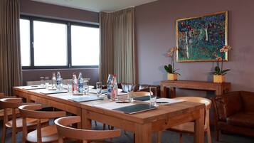 Ein Konferenzraum mit einem langen Holztisch, mehreren Stühlen und einem Bild an der Wand.