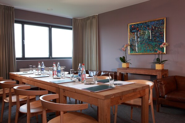 A conference room with a long wooden table, multiple chairs, and a painting on the wall.