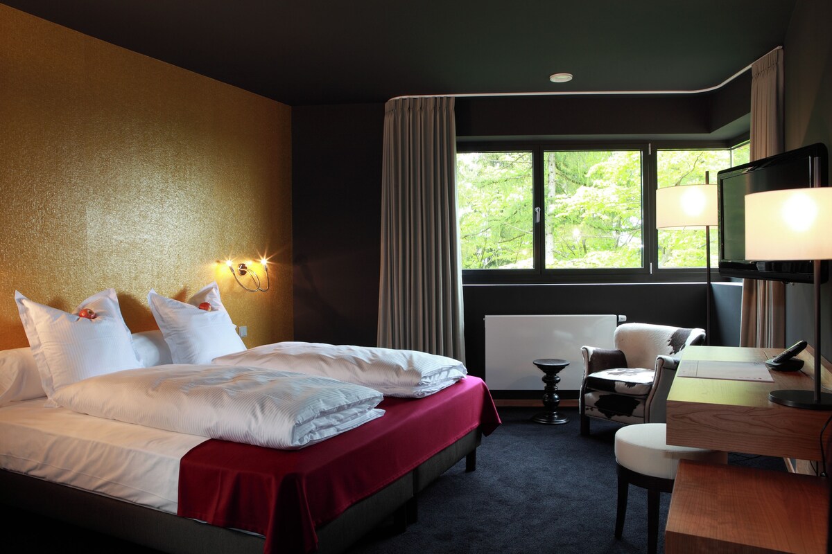 A hotel room with a bed, a desk, a chair, a TV, and a window with curtains.