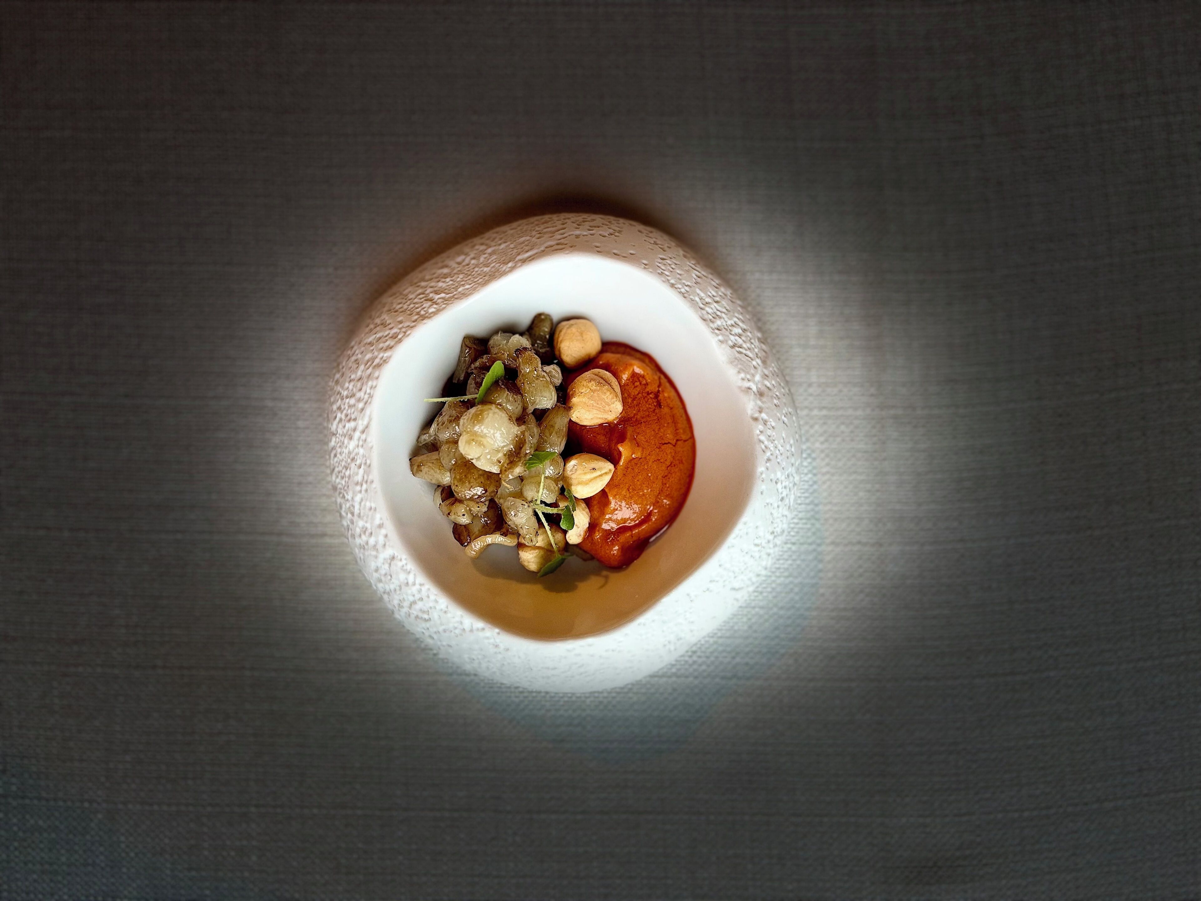 A bowl of food with nuts and seeds on a textured surface.
