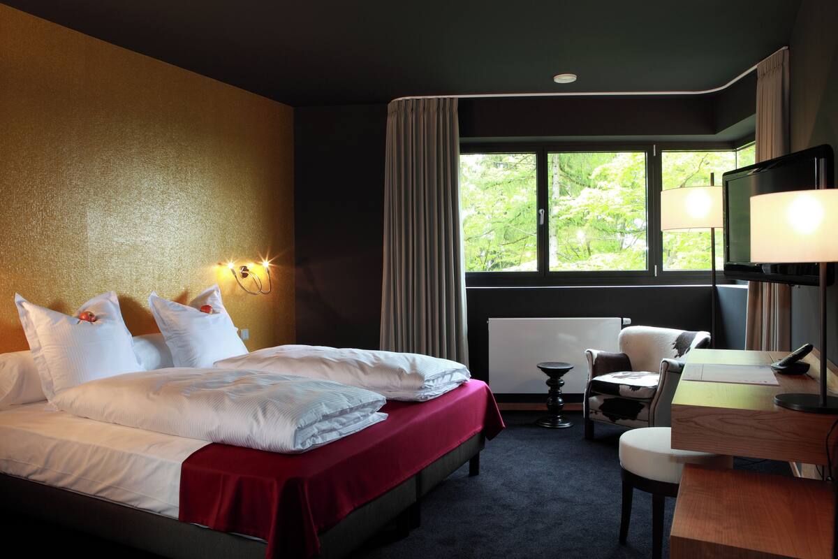 A hotel room with a bed, a desk, a chair, a TV, and a window with curtains.