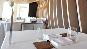 A dining area with a modern, curved wooden ceiling and a table set for two with a white tablecloth, a wooden board, and clear glassware. - The Seven Hotel (Esch-sur-Alzette)