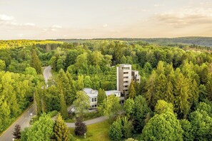 A modern building surrounded by dense forest, with a road leading to it.