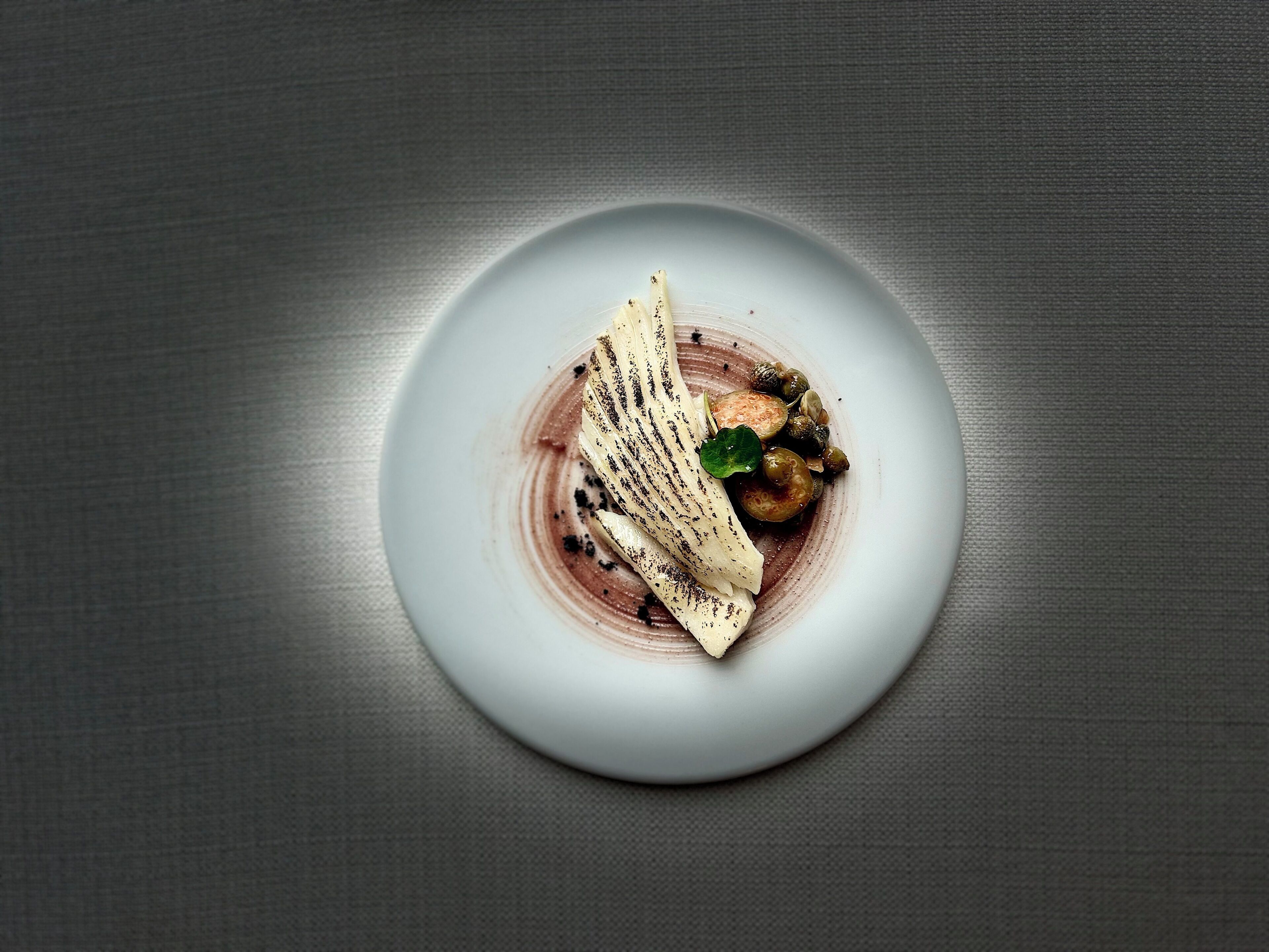 A plate with a dessert consisting of a banana, grapes, and a green leaf garnish.