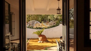 Un umbral abierto que da a un patio con una maceta, un farol colgante y vistas de un jardín con una fuente.