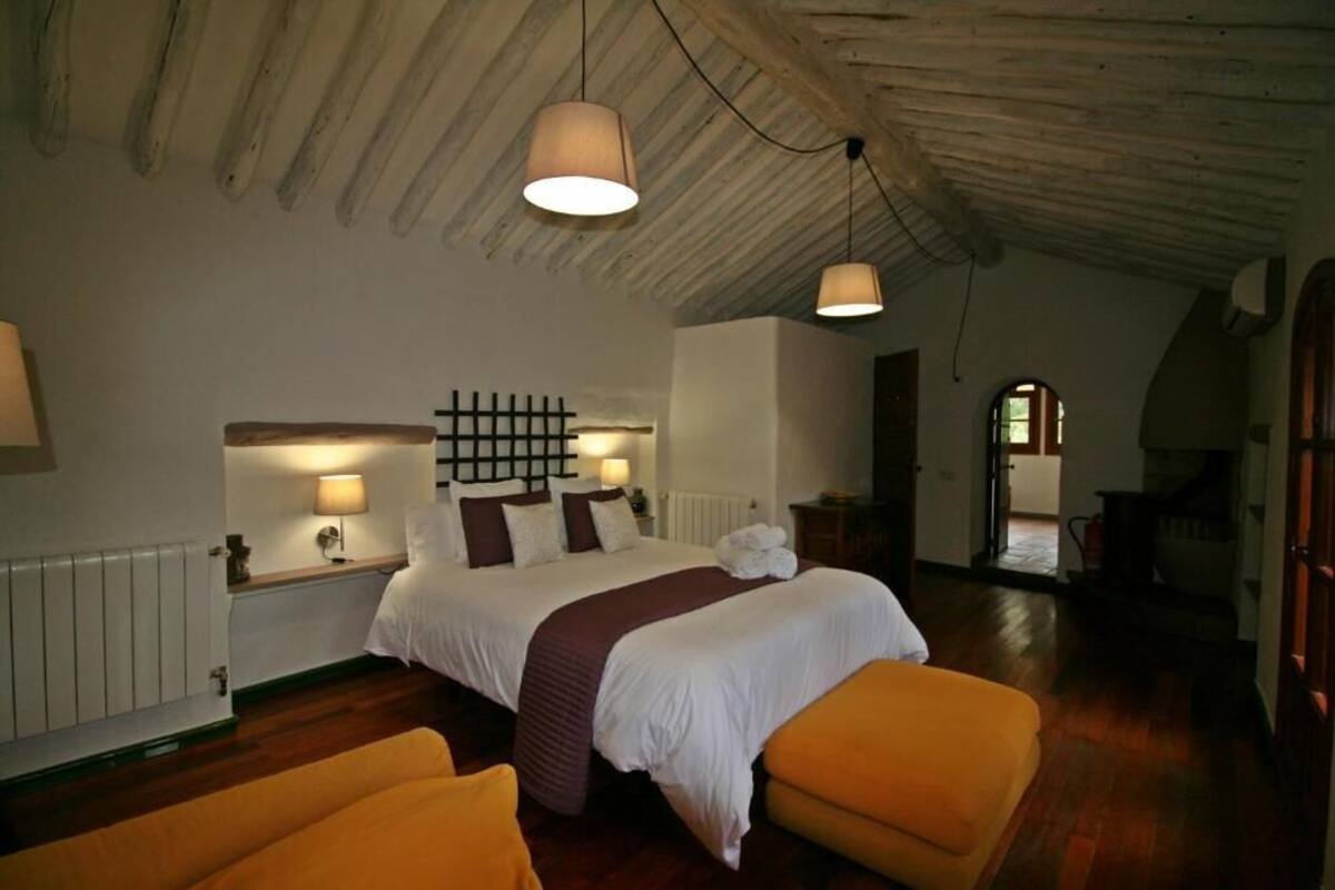 A bedroom with a large bed, two bedside lamps, a wooden ceiling, and a view of a hallway.