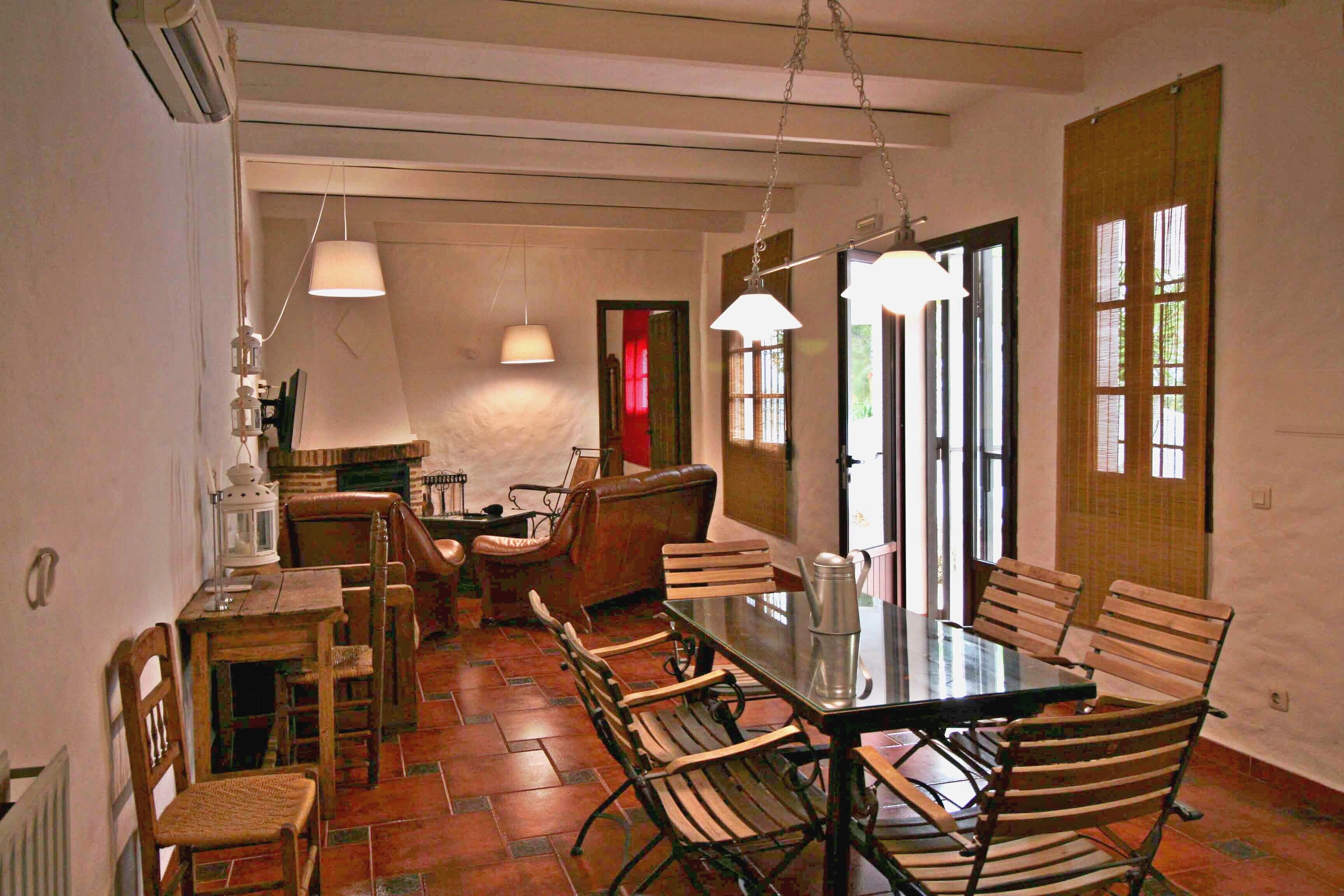 A dining area with a wooden table and chairs, a hanging light fixture, and a view of the outside through a window.