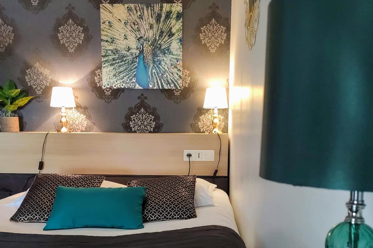 A hotel room with a bed, two bedside lamps, a decorative wall, and a green lamp on a table.