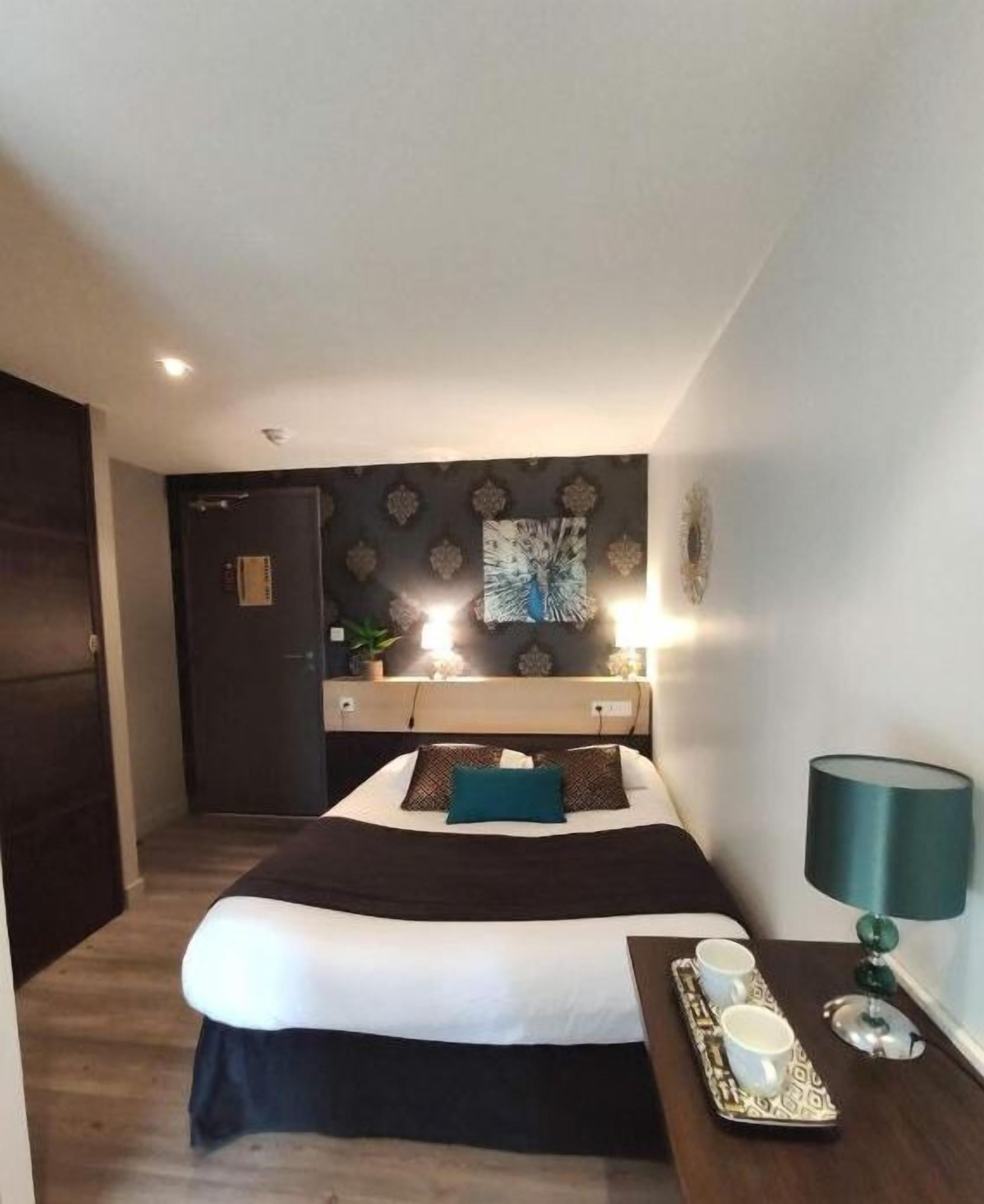 A bedroom with a bed, bedside table, lamp, and a wall-mounted artwork.
