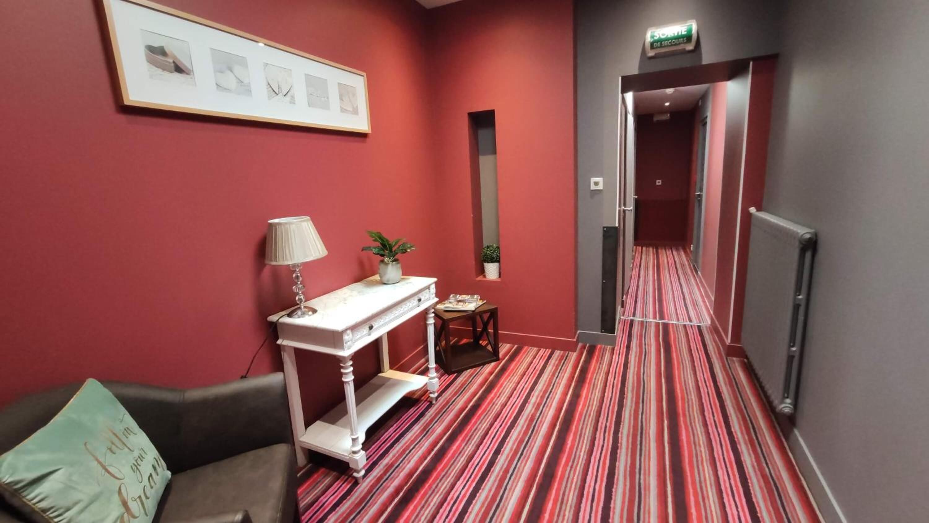 A hotel lobby with a red carpet, a white console table with a lamp, a small plant, and a framed picture on the wall.