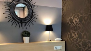 Ein Schlafzimmer mit einem Bett, zwei Kissen, einer Nachttischlampe, einem Wandspiegel und einer kleinen Topfpflanze.