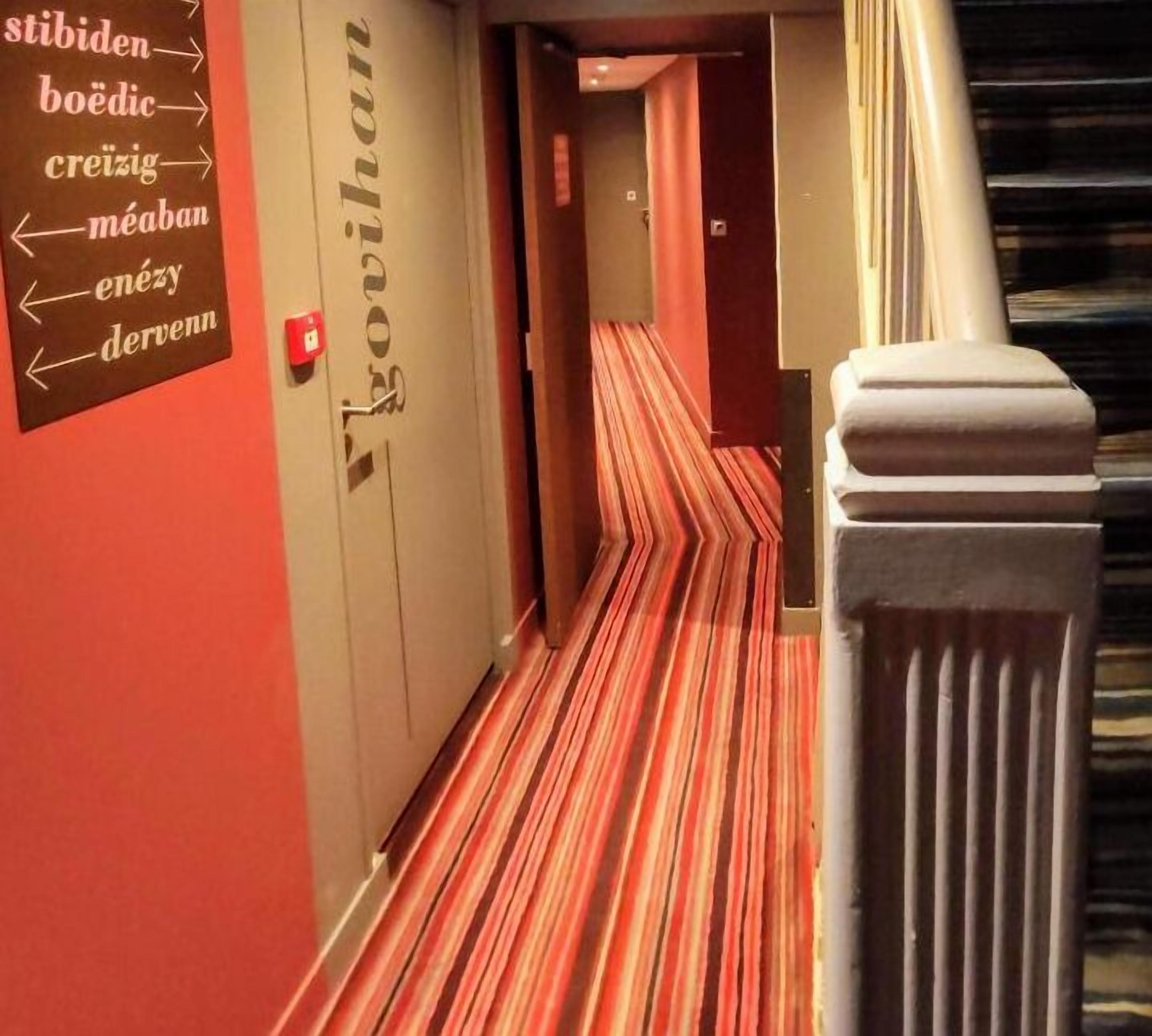 Un pasillo de hotel con alfombra a rayas y señales direccionales en las paredes.