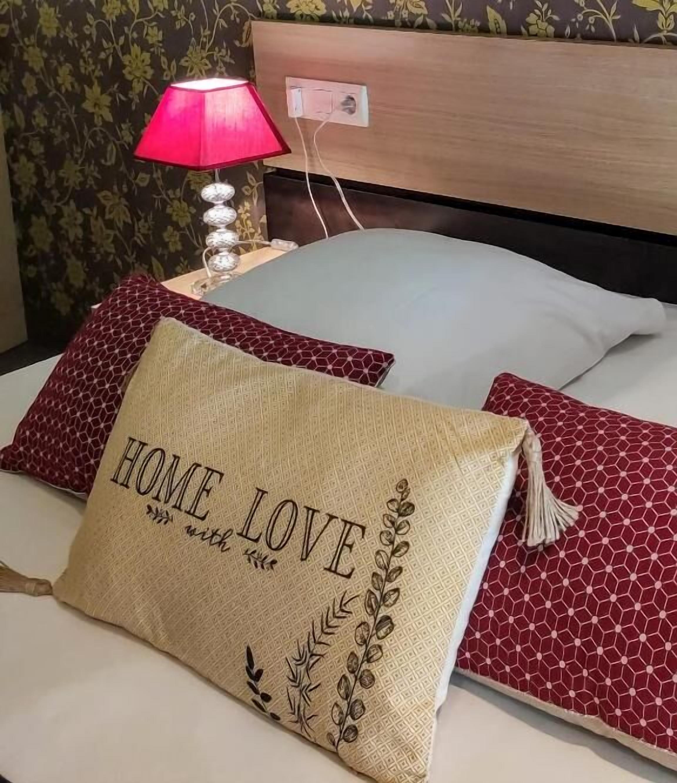 Una cama con dos almohadas, una con el texto 'HOME LOVE', una almohada estampada en rojo y una almohada blanca.