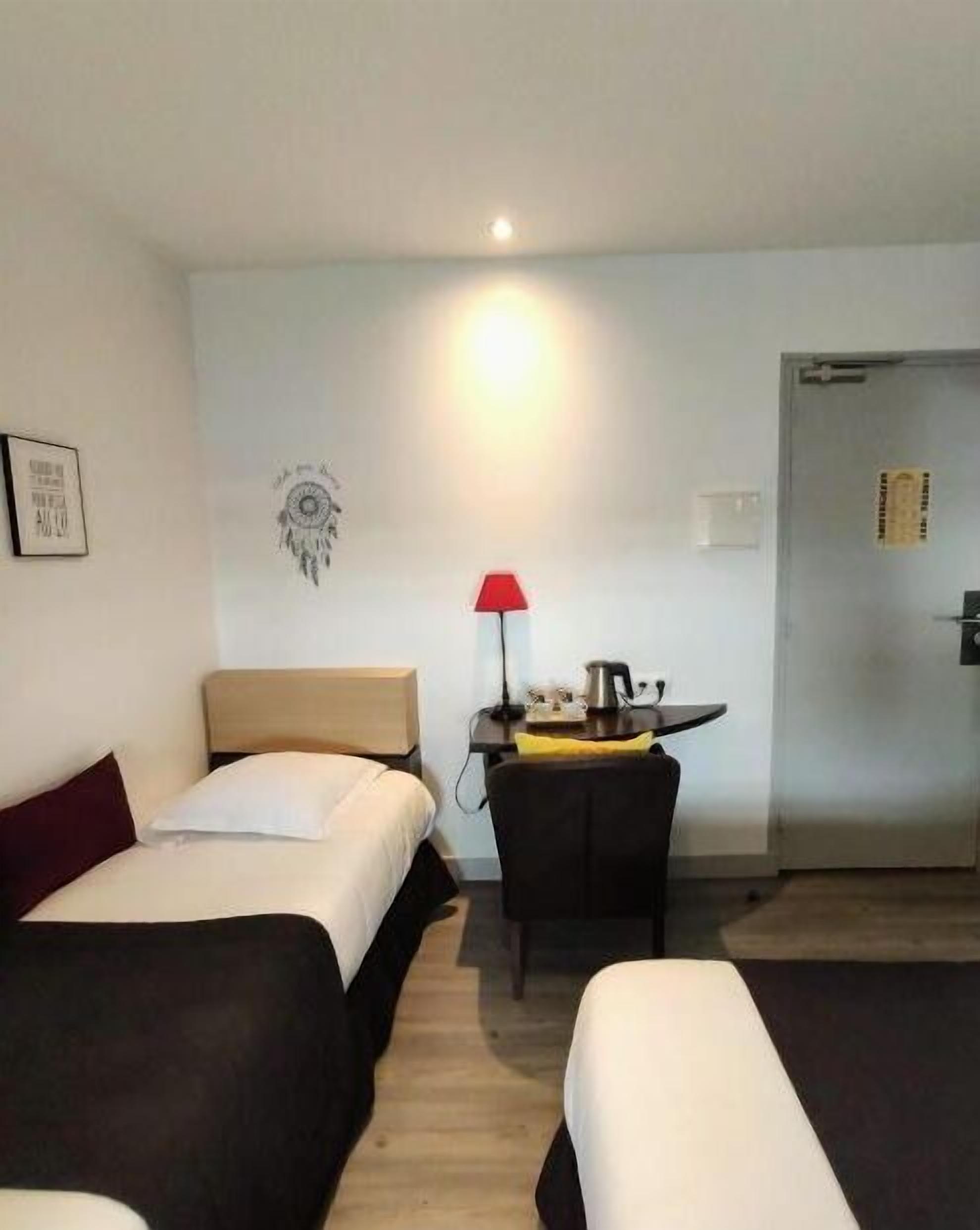 Une chambre d’hôtel avec deux lits, un bureau avec une lampe et une porte.