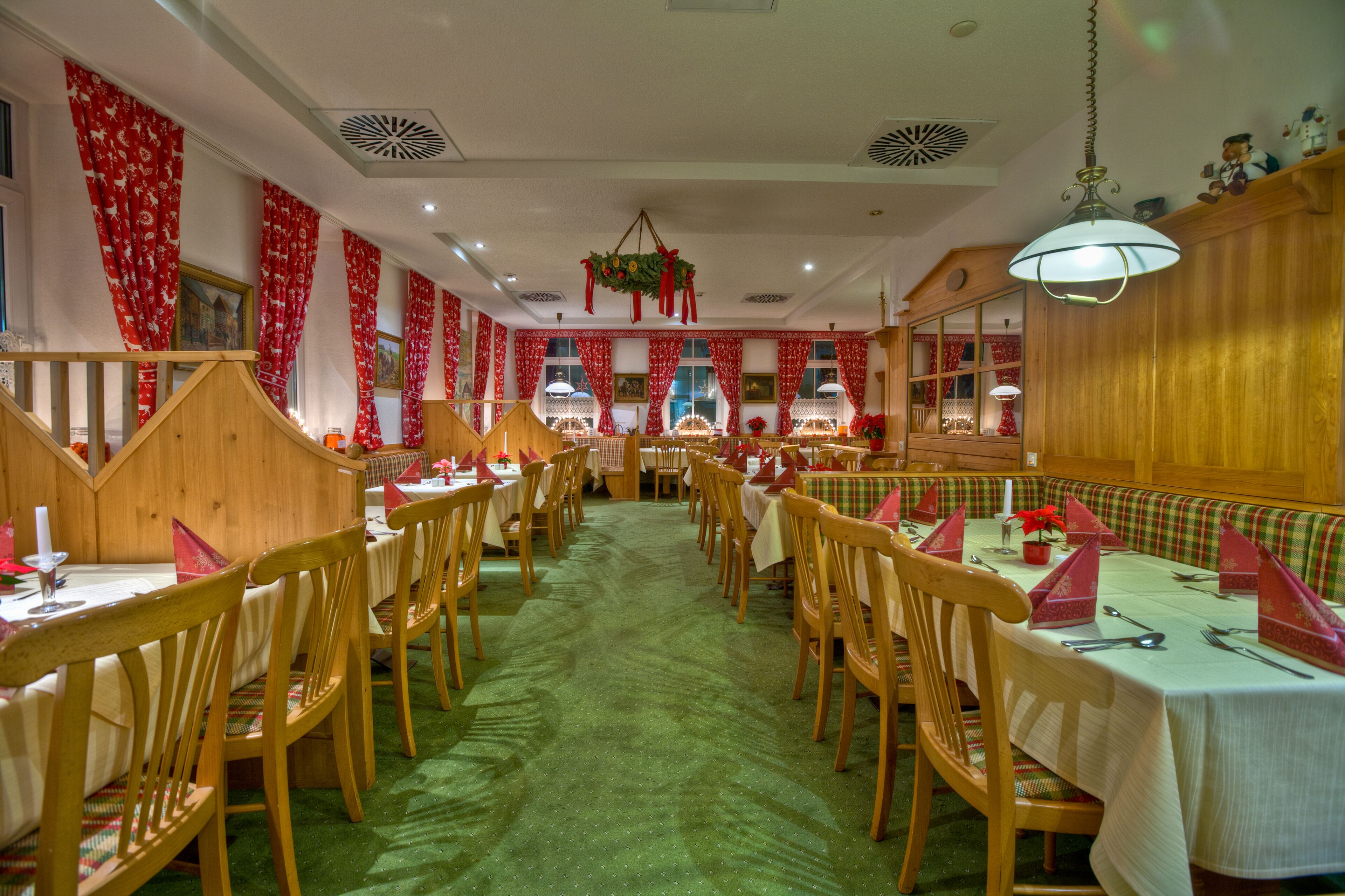 A restaurant with wooden booths and tables, red curtains, and a green carpet.