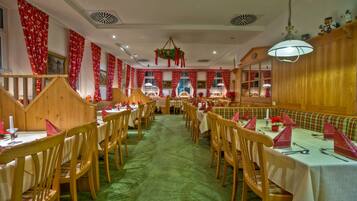 A restaurant with wooden booths and tables, red curtains, and a green carpet.