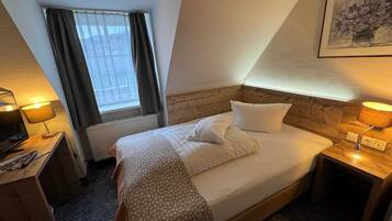 Una camera d'albergo con un letto, una scrivania, una lampada, una finestra con tende e un quadro appeso al muro.