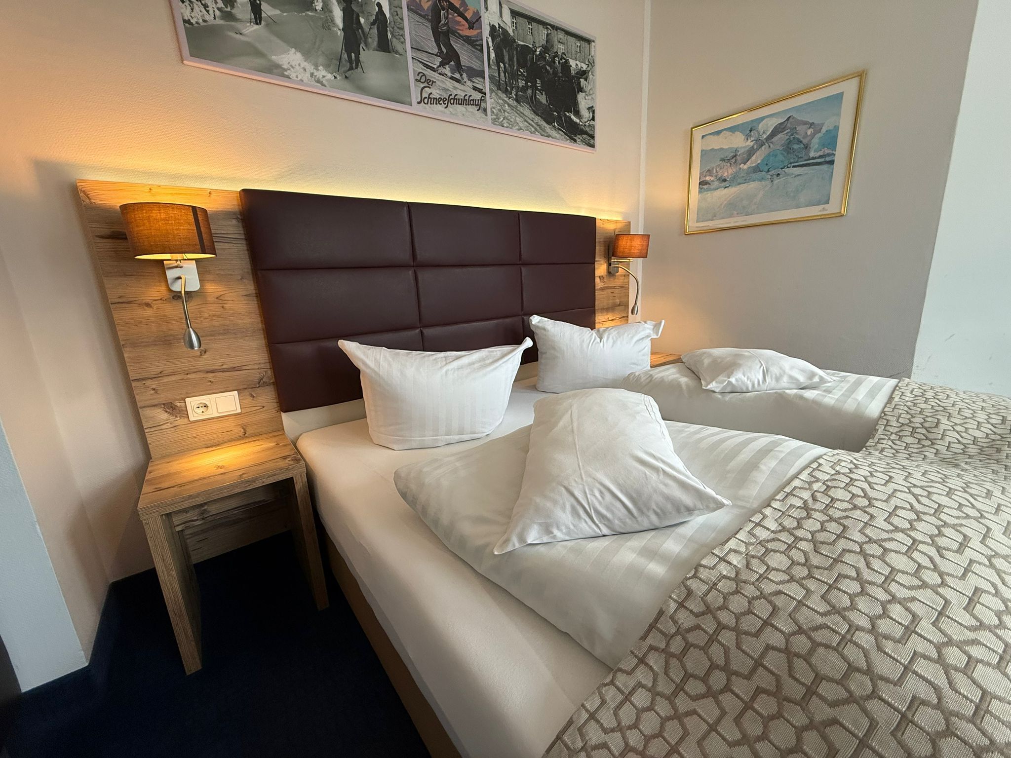 A hotel room with a large bed, two bedside tables, a headboard, and wall-mounted lamps.