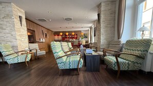 Un amplio salón con suelo de madera, una zona de bar con detalles rojos y sillones con estampado.