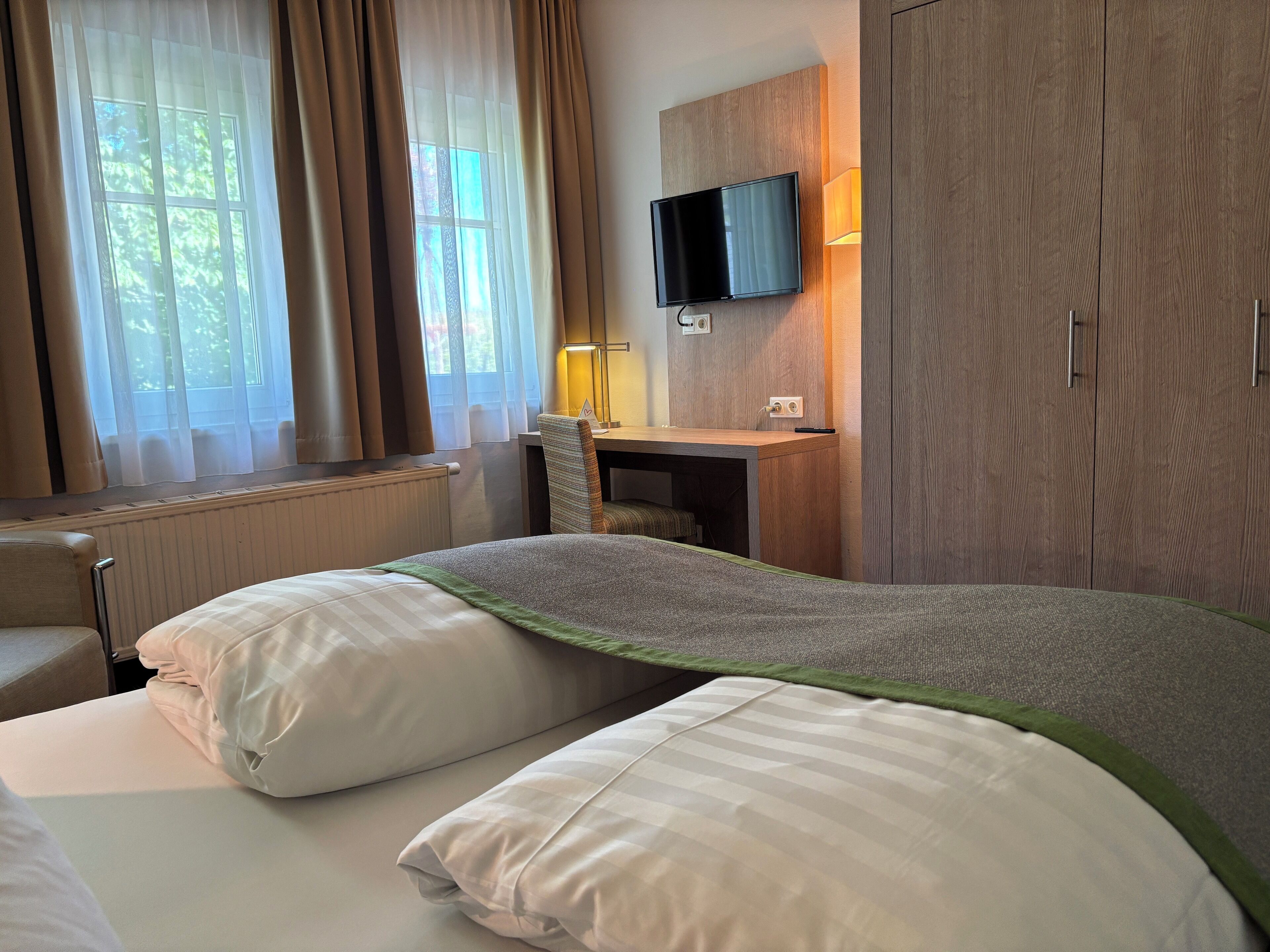 Una camera d'albergo con un letto, una scrivania, una televisione e un armadio.