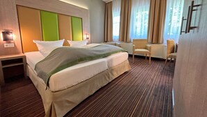 Una habitación de hotel con una cama grande, una mesita de noche, una silla y una ventana con cortinas.