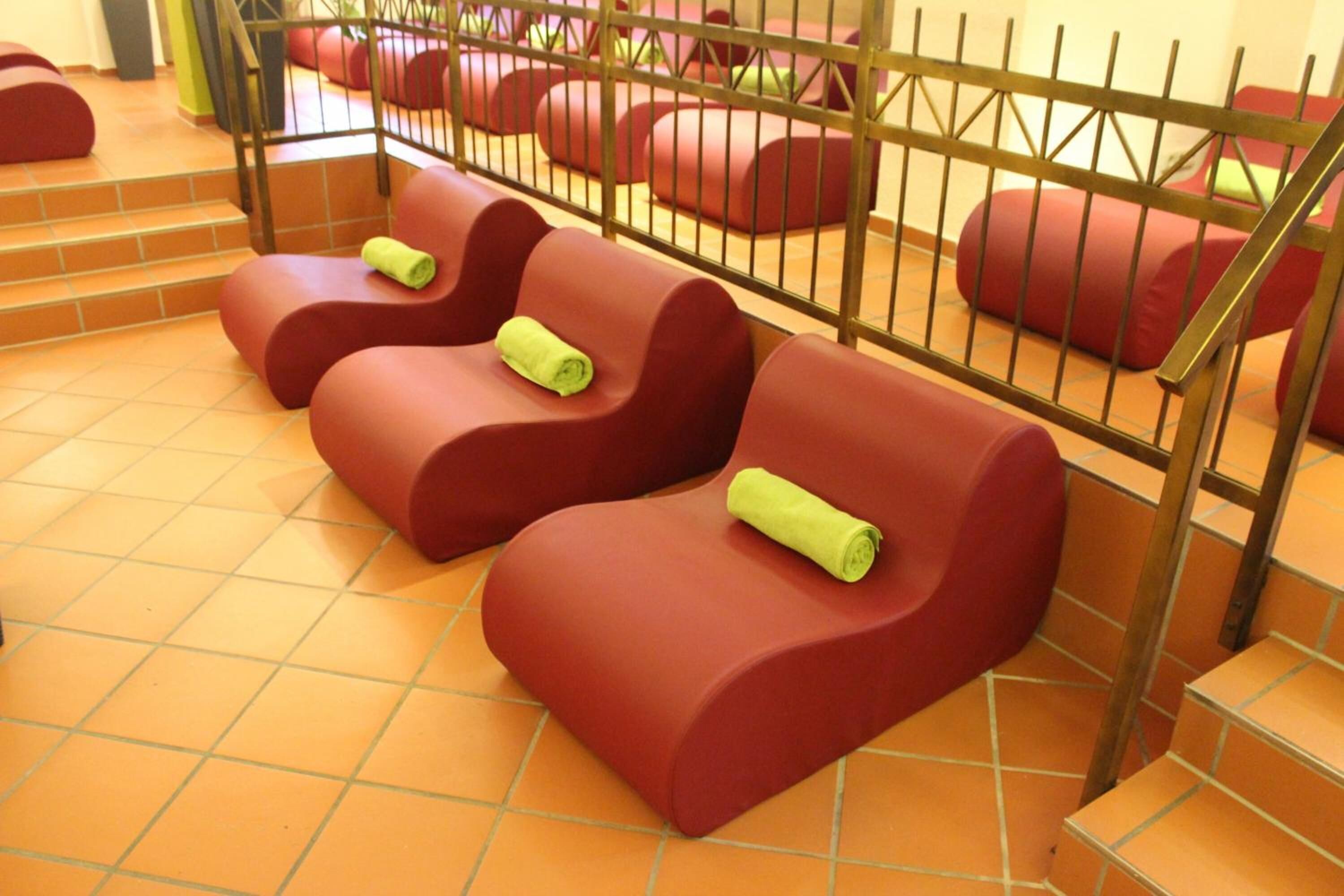 A row of red cushioned seating areas with green towels, separated by a metal fence, and a tiled floor.