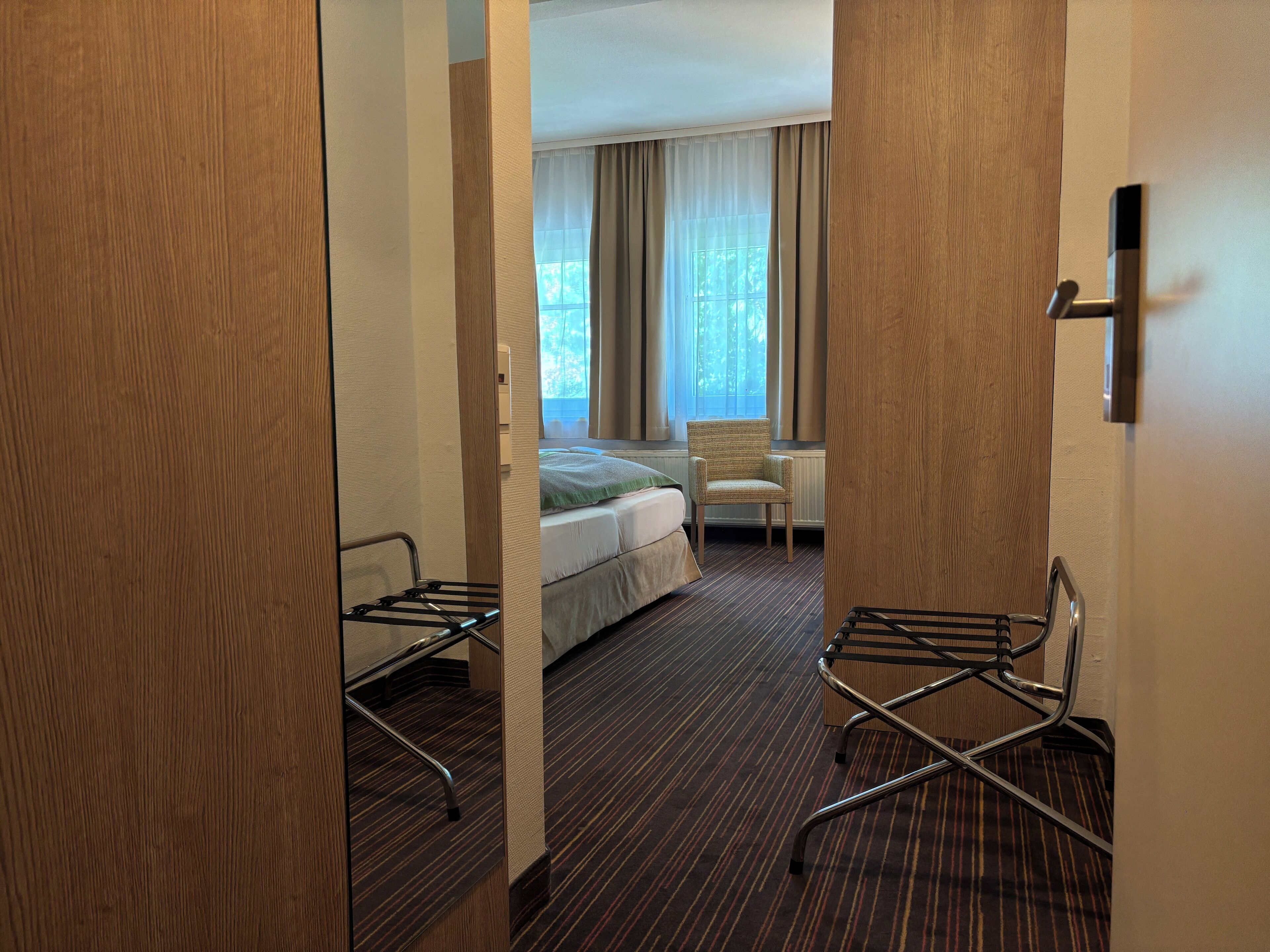 Een hotelkamer met een bed, een stoel, een bureau en een raam met gordijnen.