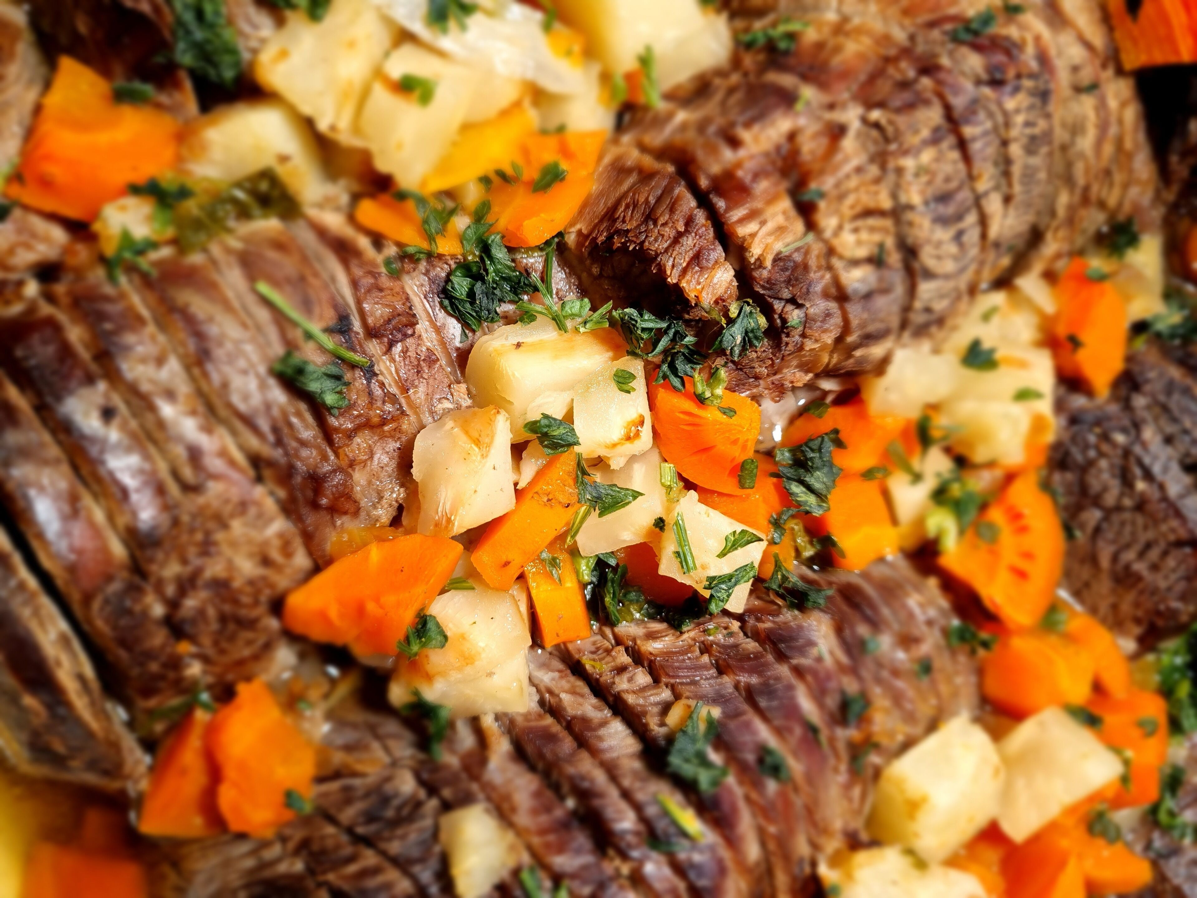 A close-up of a cooked dish with sliced meat, diced potatoes, and carrots, garnished with herbs.