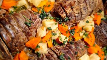 A close-up of a cooked dish with sliced meat, diced potatoes, and carrots, garnished with herbs.