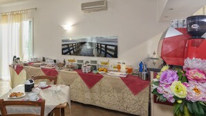 A breakfast setup with a table covered in a red tablecloth, a coffee machine, and a painting of a pier on the wall. - Eden Park Resort (San Giuliano Terme)