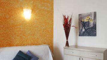 A room with a sofa, a vase with dried plants, a wall-mounted light, and a framed picture.
