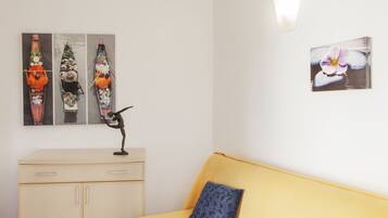 A room with a yellow sofa, a wooden cabinet, and three wall-mounted artworks depicting boats and a flower.