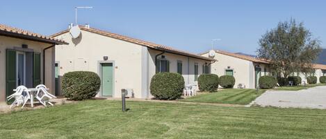 A row of single-story buildings with a consistent architectural style, featuring a tiled roof and a small front yard with a lawn and a few potted plants.