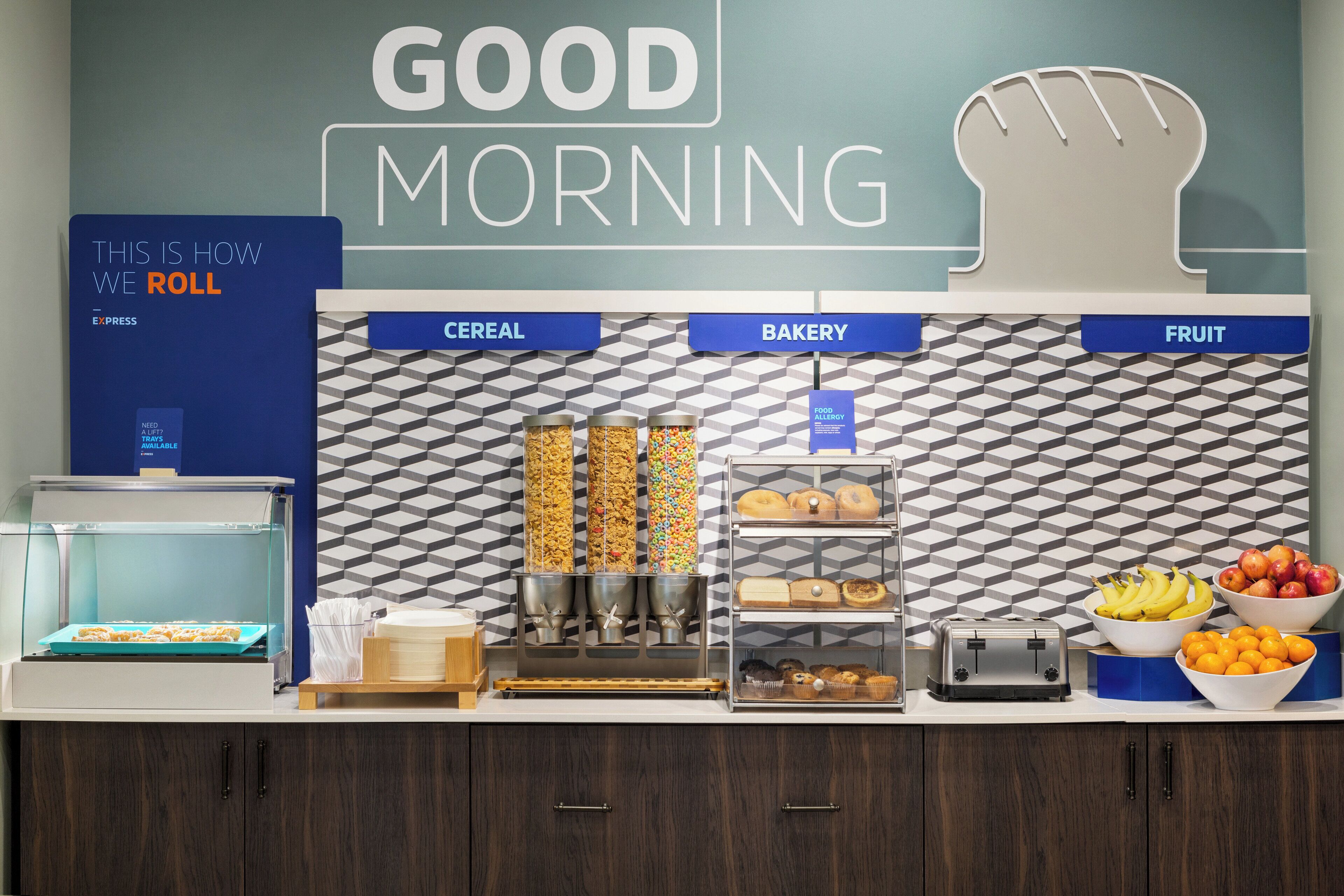 A breakfast buffet area with labeled sections for cereal, bakery, and fruit.