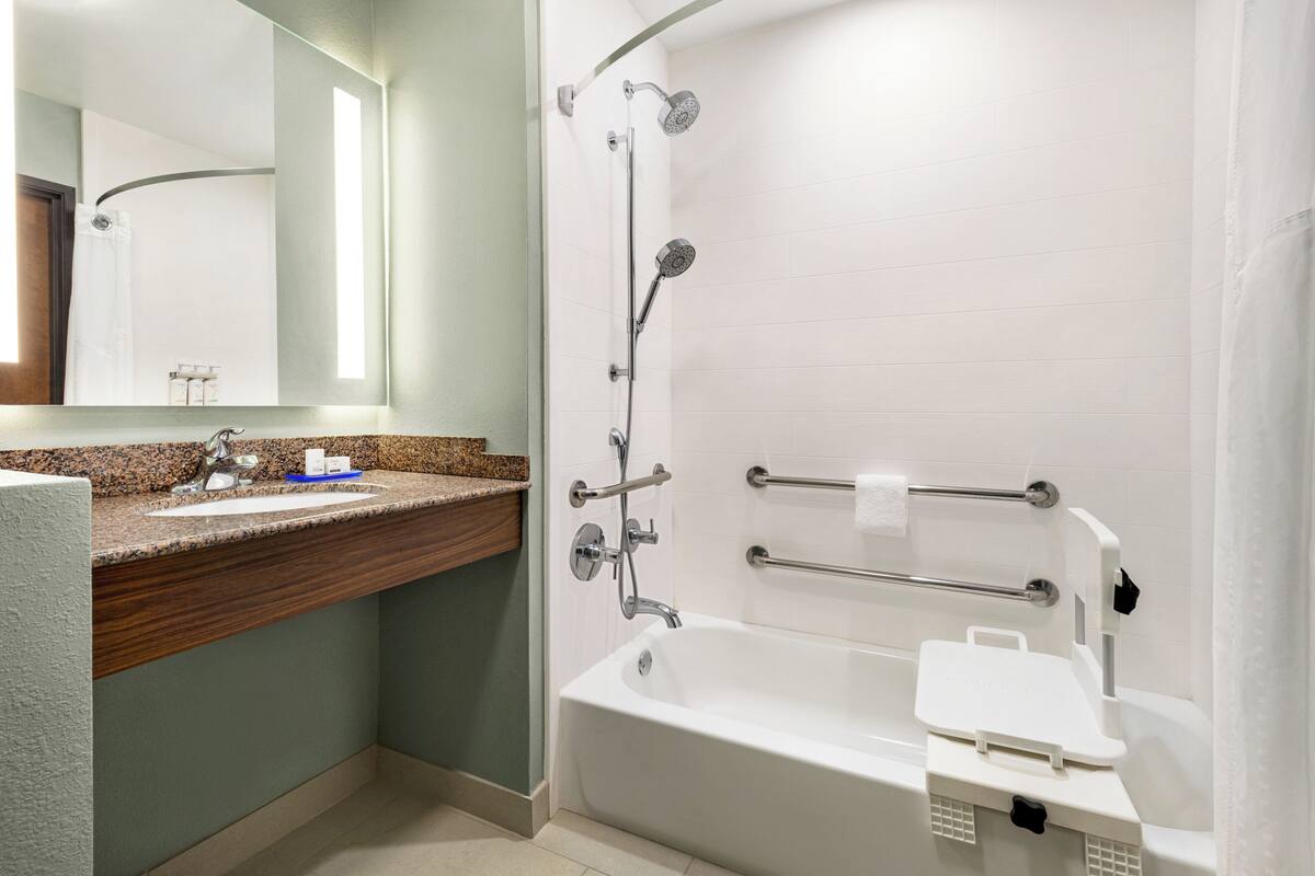 A modern bathroom with a white bathtub, a granite countertop sink, and a shower with a handheld showerhead.