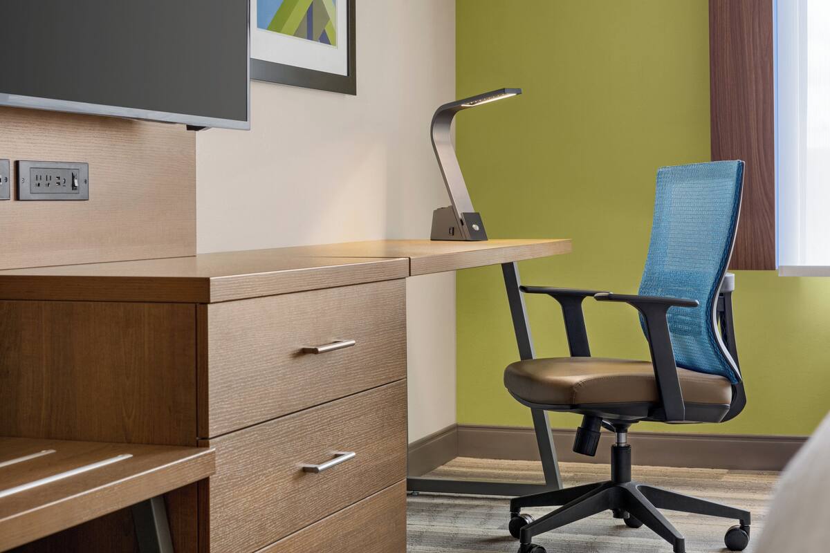 A modern office space with a wooden desk, a blue office chair, a standing lamp, and a framed picture on the wall.