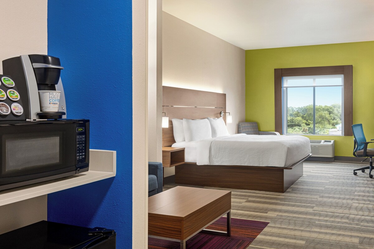 Habitación de hotel con cama, escritorio, microondas, cafetera y ventana con vista a árboles.