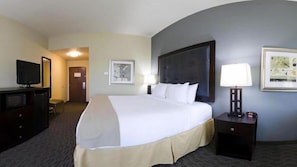 Une chambre d’hôtel avec un grand lit, un téléviseur posé sur une commode, un bureau et un tableau encadré au mur.