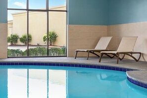 Zona de piscina amb una cadira relaxant, vista d'un edifici amb façana groga i vora de piscina amb rajoles.