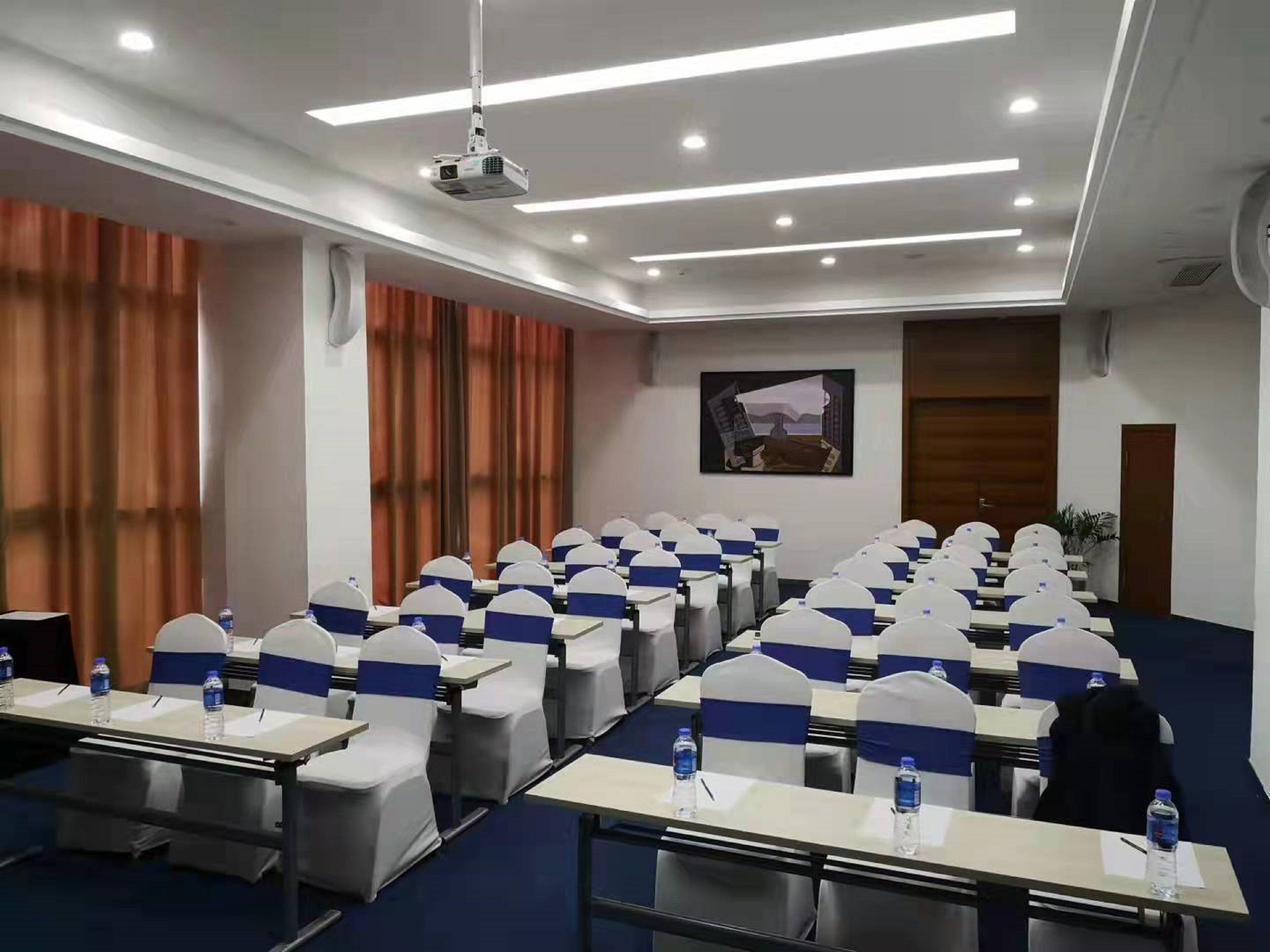 A conference room with rows of tables and chairs, a projector, and a painting on the wall.