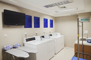 A laundry facility with multiple washing machines, a table with an iron, and instructional signs on the wall. - Holiday Inn Express Suzhou Changjiang by IHG (Suzhou)